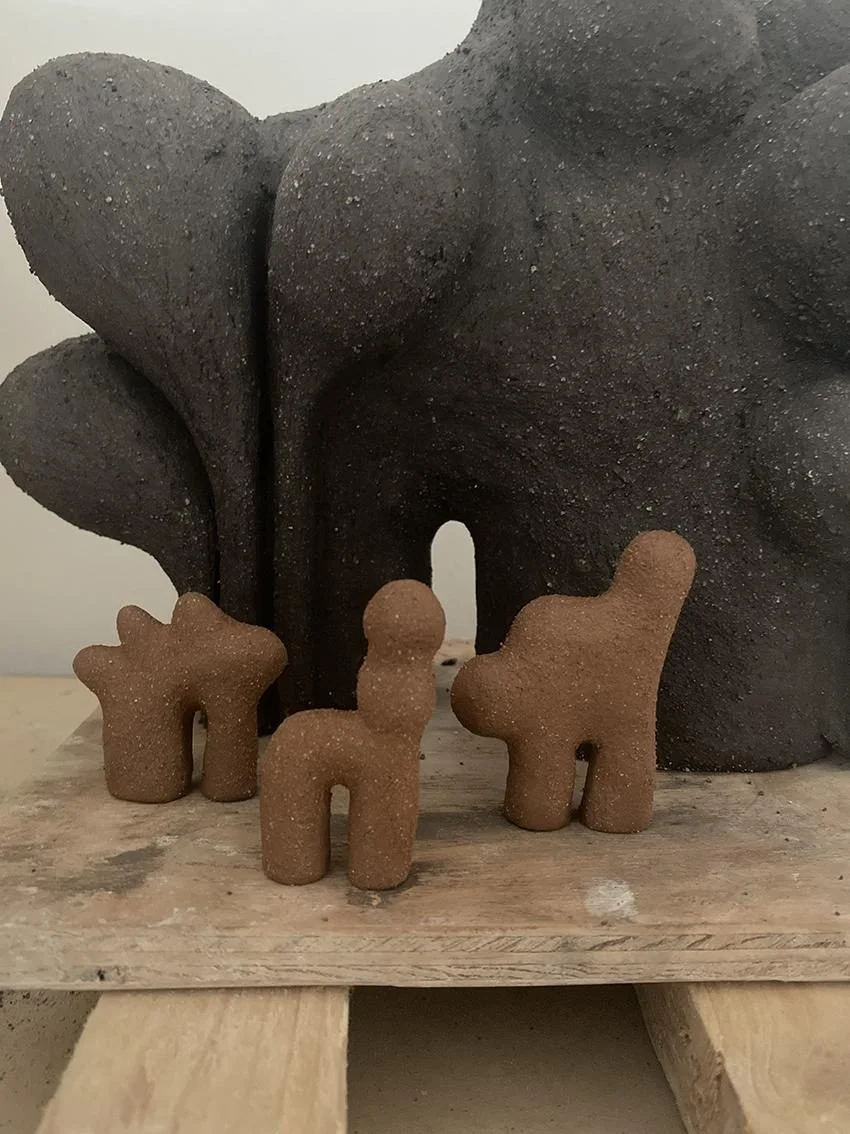 Amulettes d'Elisa Uberti, trois petites figurines en grès brun aux silhouettes animales stylisées, posées devant la sculpture Nature Boy en grès noir.