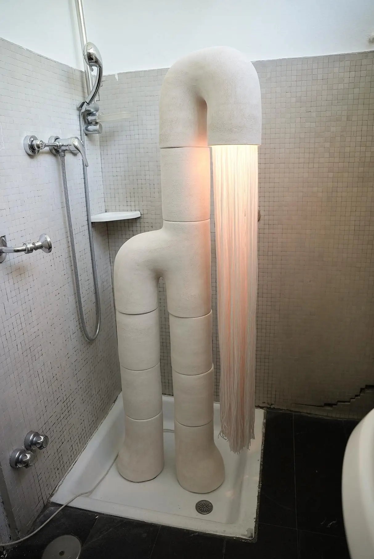 Fontaine #4 d'Elisa Uberti, sculpture lumineuse en grès blanc à la silhouette bipède, longue chevelure de franges éclairée installée dans une salle de bain.