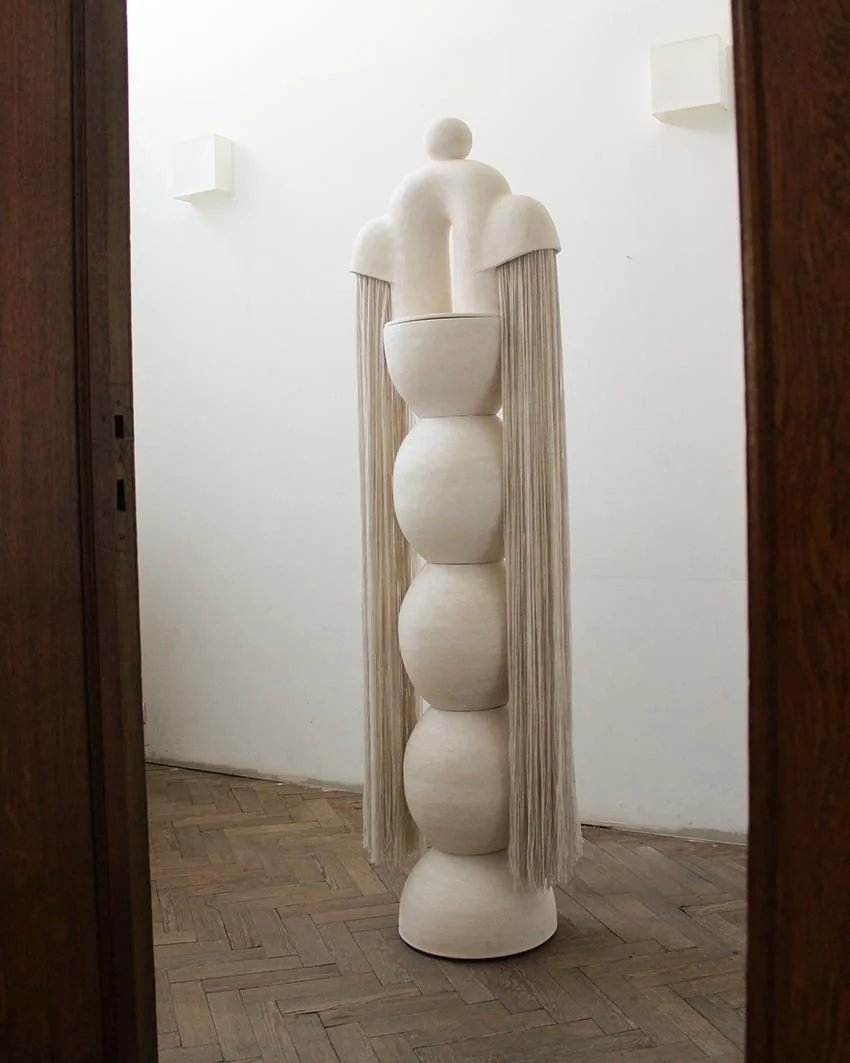 Fontaine de Jouvence #4 d'Elisa Uberti, sculpture lumineuse en grès blanc composée de sphères empilées et couronnée d'une arche, avec de longues franges de laine crème retombant de chaque côté.